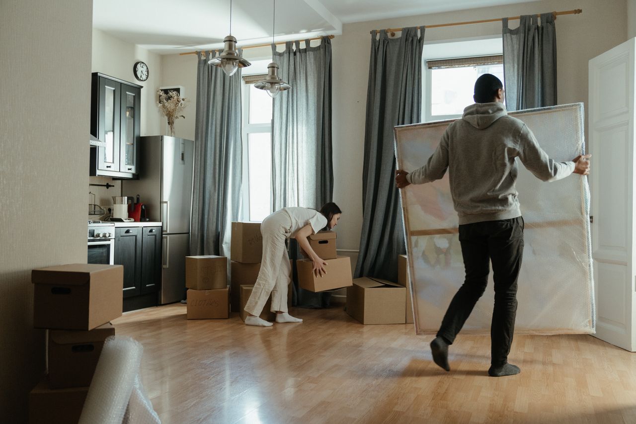 our-story A young couple unpacks boxes in their new apartment, arranging their belongings.