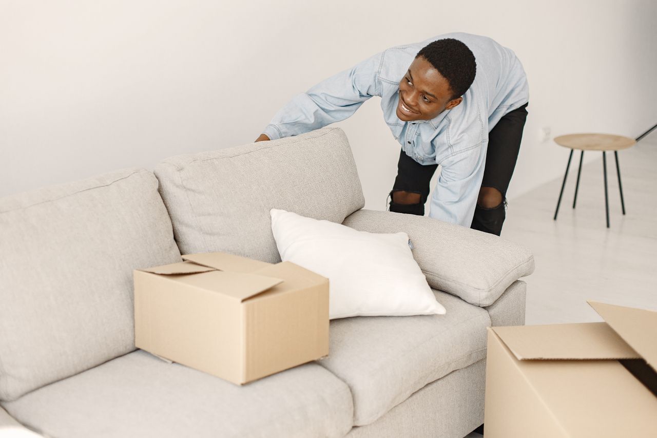 creative-02 Young man smiling while arranging cardboard boxes in a modern living room.